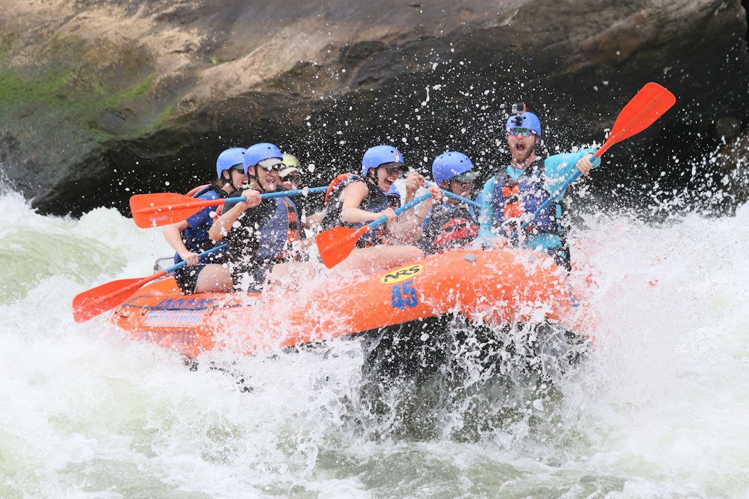 Experiencing an amazing activity of whitewater rafting on the New River Gorge in West Virginia. Great family-friendly fun and heart-racing adventure. It's the ultimate outdoor experience. by Florida Getaways people riding orange kayak on water during daytime