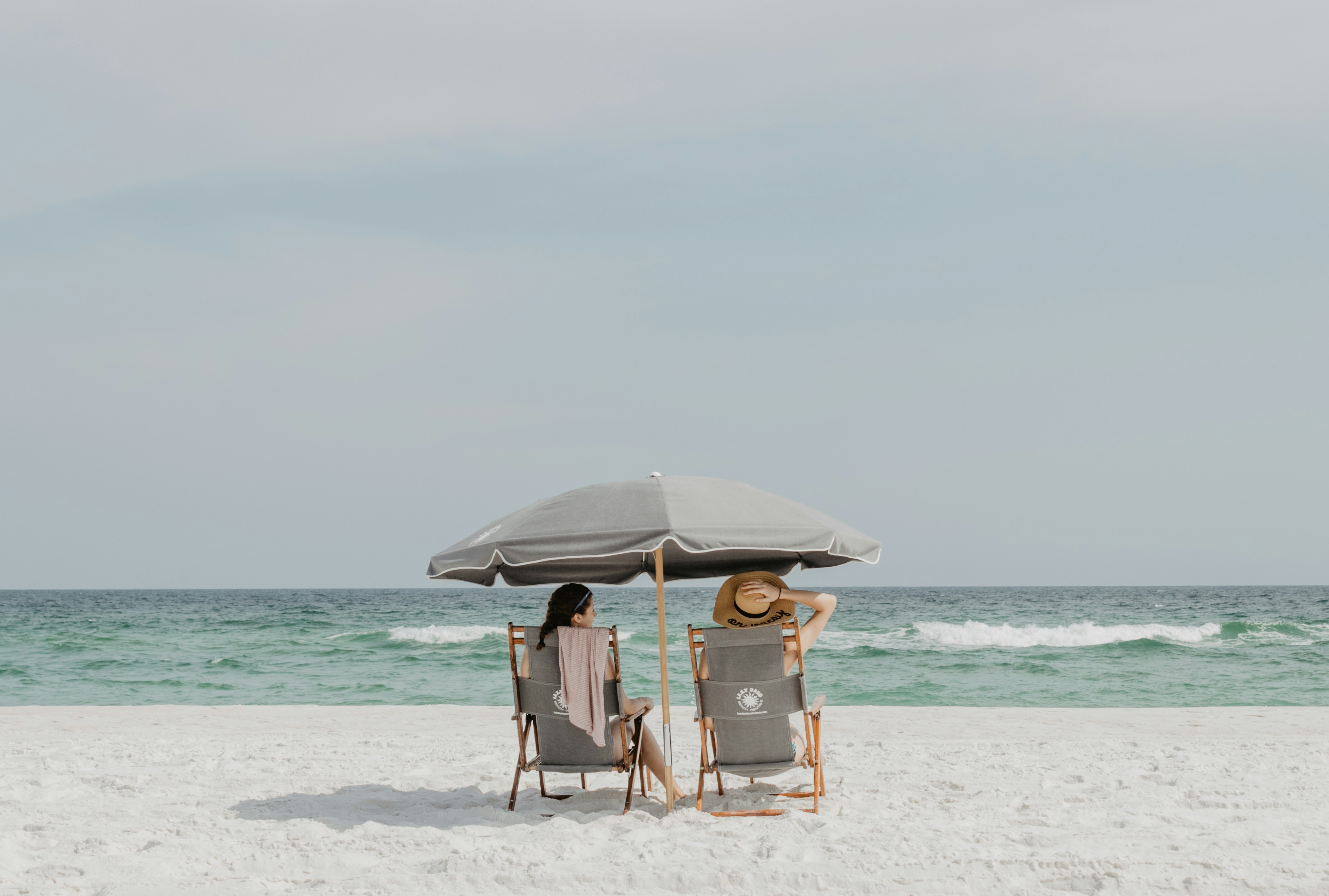 Just another day at the beach. by Florida Getaways two people under beach umbrella near shoreline
